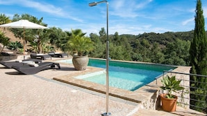A swimming pool with lounge chairs and potted plants, surrounded by a stone patio and a scenic hillside view. - Holiday Home Casa L (Sao Bras de Alportel)