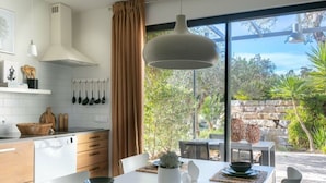 A modern kitchen with white cabinets, a white countertop, and a dining area with a table set for two. - Holiday Home Casa L (Sao Bras de Alportel)