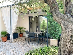 Une terrasse avec une table et des chaises, entourée de plantes en pot et d’un arbre.
