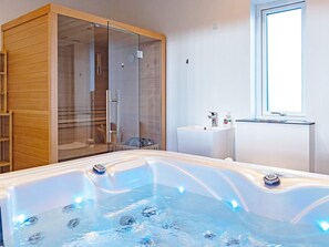 A modern bathroom with a glass-enclosed shower, a large bathtub with jets, and a window providing natural light.