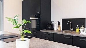 A modern kitchen with dark cabinetry, a built-in oven, a coffee maker, and a sink with a faucet. - 9 Person Holiday Home in Vaeggerlose (Vaeggerlose)