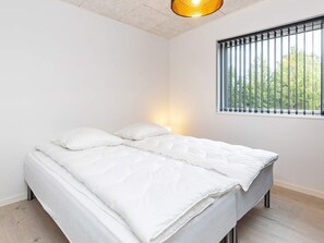 A bedroom with a bed, a window with blinds, a ceiling light, and a view of greenery outside. - 9 Person Holiday Home in Vaeggerlose (Vaeggerlose)
