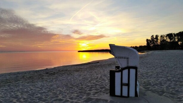 A beach chair on a sandy shore with a sunset in the background. - Waldhaus No.15 Modern Retreat (Monkebude)