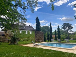 A swimming pool with lounge chairs, a stone wall, and a house with ivy-covered walls. - La Clé des Champs in Barbat, Nature-Filled Home with Pool in a Wooded Park (Savignac)