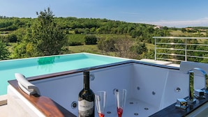 A poolside area with a jacuzzi, a bottle of wine, and two glasses. - Villa Zvonar Comfortable Holiday Residence (Karojba)