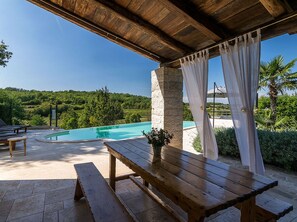 Ein Sitzbereich im Freien aus Holz mit Pool und Blick auf eine üppige Landschaft.