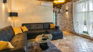 A modern living room with a black leather sectional sofa, a glass coffee table, and a stone wall. - Villa Zvonar Comfortable Holiday Residence (Karojba)
