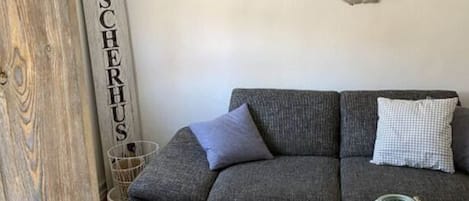 A living room with a grey sofa, two round side tables, a decorative wall piece, and a vertical sign.