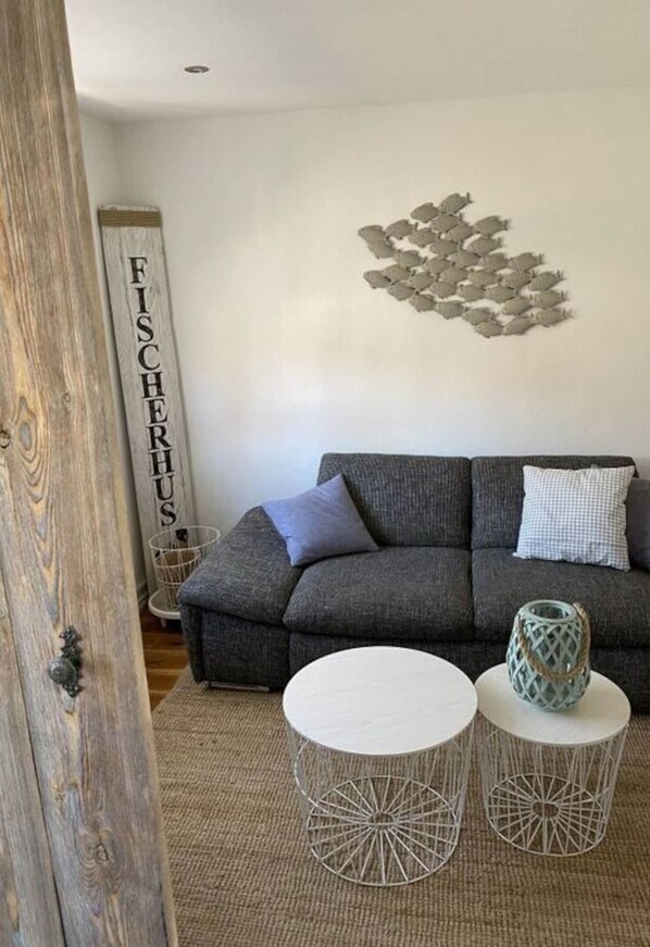 Un salon avec un canapé gris, deux petites tables d’appoint rondes, un élément décoratif mural et un panneau vertical.