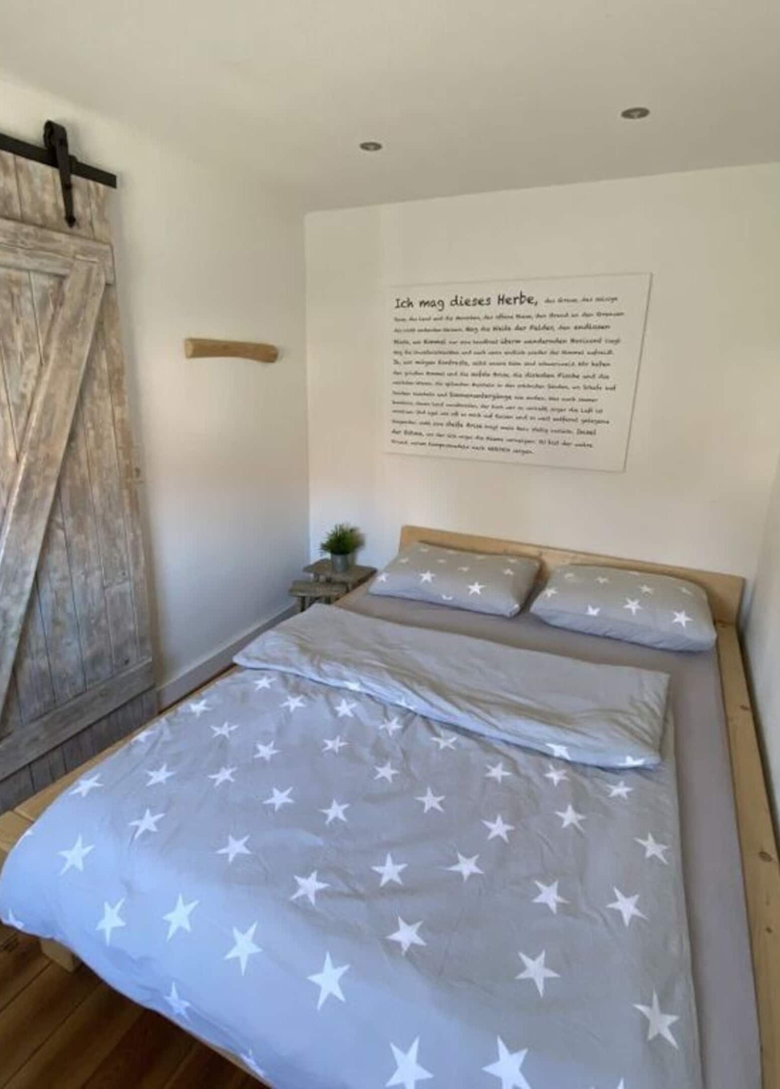 Une chambre à coucher comprenant un lit, une tête de lit en bois, une étagère fixée au mur et un élément décoratif mural avec du texte.