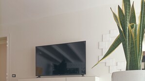 Ein modernes Wohnzimmer mit einem an der Wand befestigten Flachbildfernseher, einem weißen Sofa, einem weißen Couchtisch und einer Zimmerpflanze.