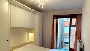 A bedroom with a bed, built-in wardrobe, and a window with a view of a brick building. - Chic Urban Seaside Apartment (Nieuwpoort)