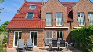 Een herenhuis met twee verdiepingen, met een rode dakbedekking, een overdekte patio met tuinmeubilair en een kleine tuin.