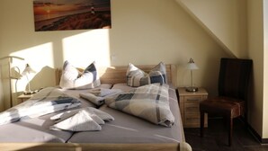 Een slaapkamer met een bed, kussens, een nachtkastje, een lamp, een stoel en een schilderij aan de muur.