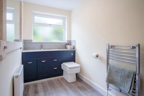A bathroom with a dark blue vanity, a white toilet, a window, and a towel rack. - Dolphin - 2 Bedroom Apartment - Saundersfoot (Saundersfoot)
