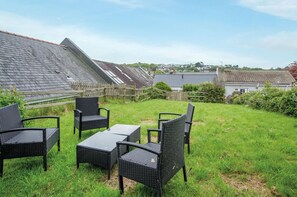 A backyard with a table and four chairs, a wooden fence, and houses in the background. - Dolphin - 2 Bedroom Apartment - Saundersfoot (Saundersfoot)