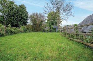 A grassy backyard with a wooden fence, a shed, and a tree.