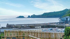 A coastal view with a wooden fence, a harbor with boats, and a building with a modern design.