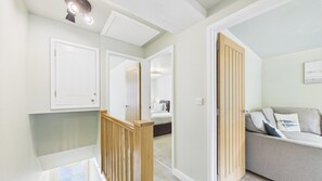 A hallway with a staircase, a wooden door, and a grey sofa with cushions. - Dolphin - 2 Bedroom Apartment - Saundersfoot (Saundersfoot)