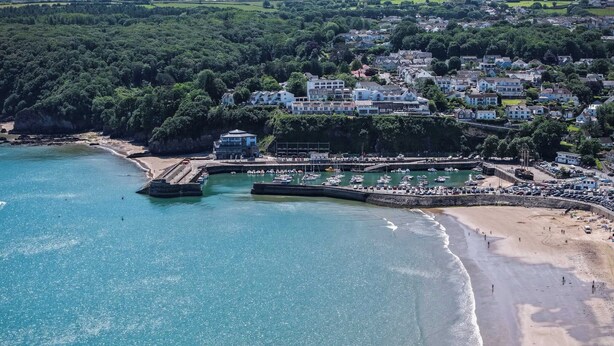 An aerial view of a coastal town with a beach, a marina, and residential buildings.