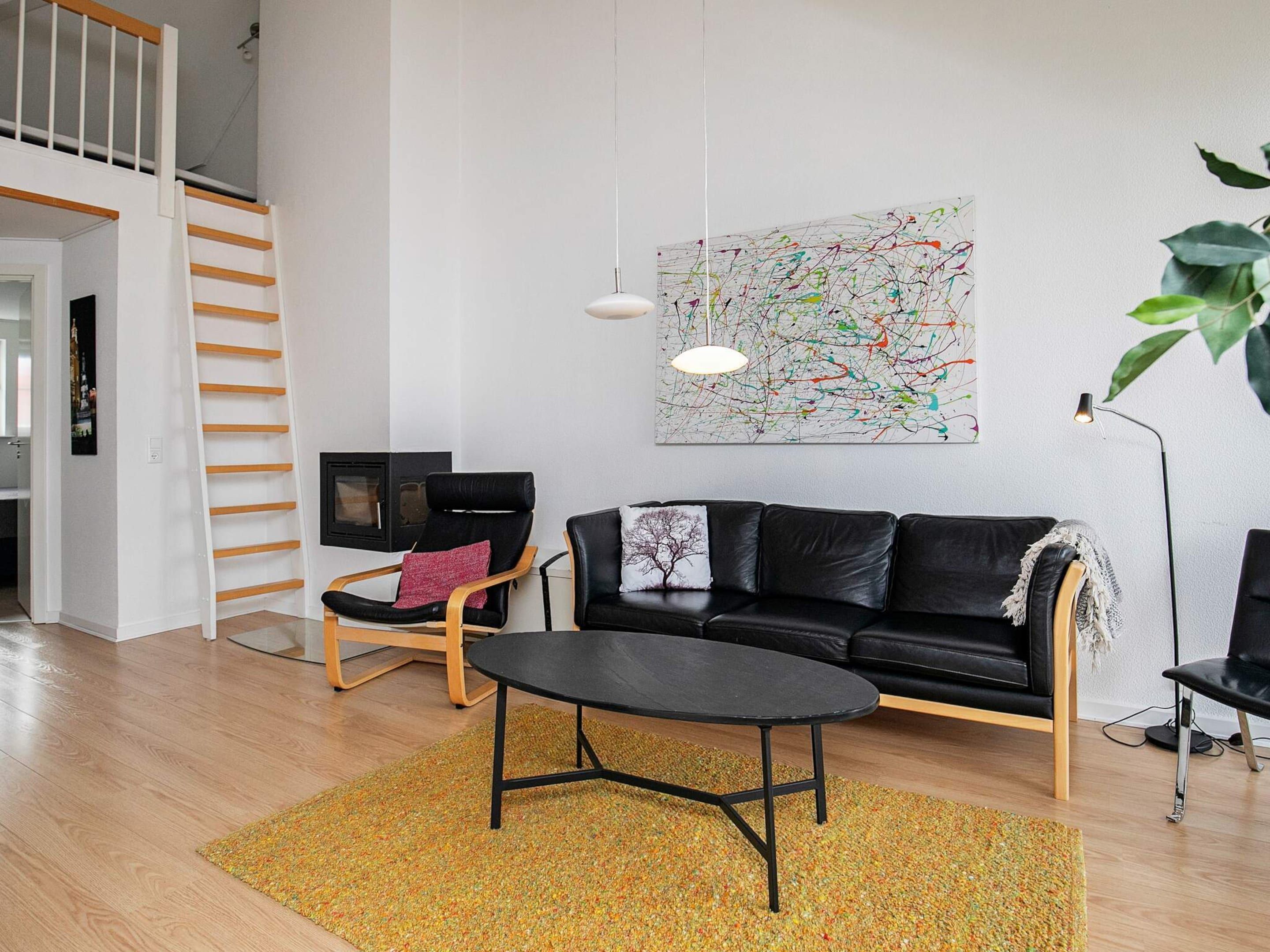 A modern living room with a black leather sofa, a wooden coffee table, a black armchair, and a colorful abstract painting on the wall.