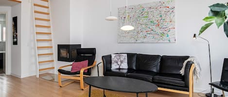 Un salon moderne avec un canapé en cuir noir, une table basse en bois, un fauteuil noir et un tableau abstrait aux couleurs vives accroché au mur.