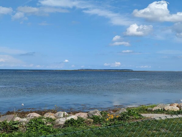 Vista costera con cielo despejado, mar tranquilo y una masa de tierra a lo lejos.