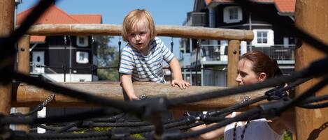 A wooden play structure with ropes and a child climbing.