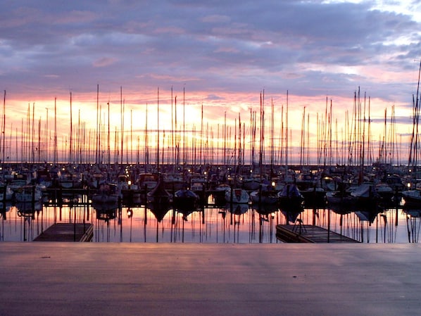 A marina with numerous boats docked at calm water reflecting the sunset sky.