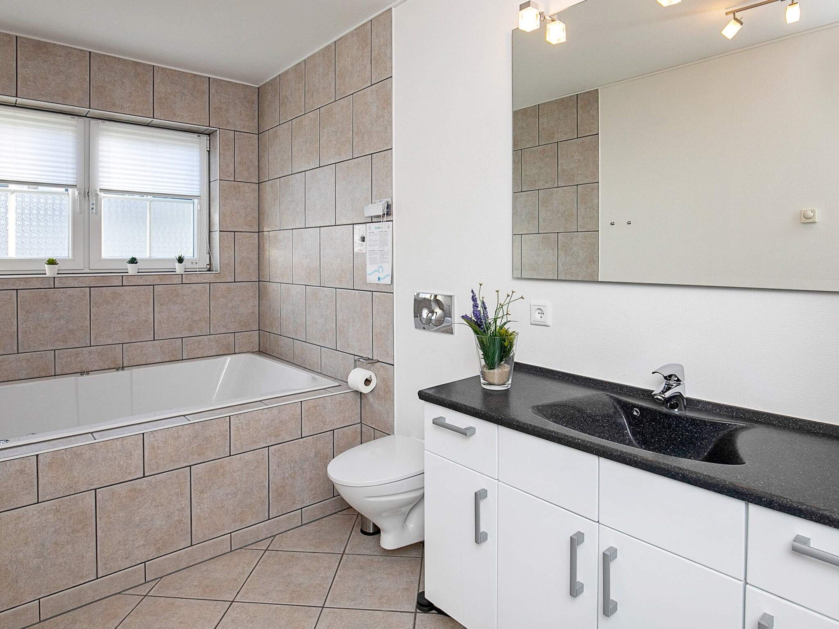 Une salle de bain moderne équipée d’une baignoire, de toilettes, d’un lavabo et d’un grand miroir.