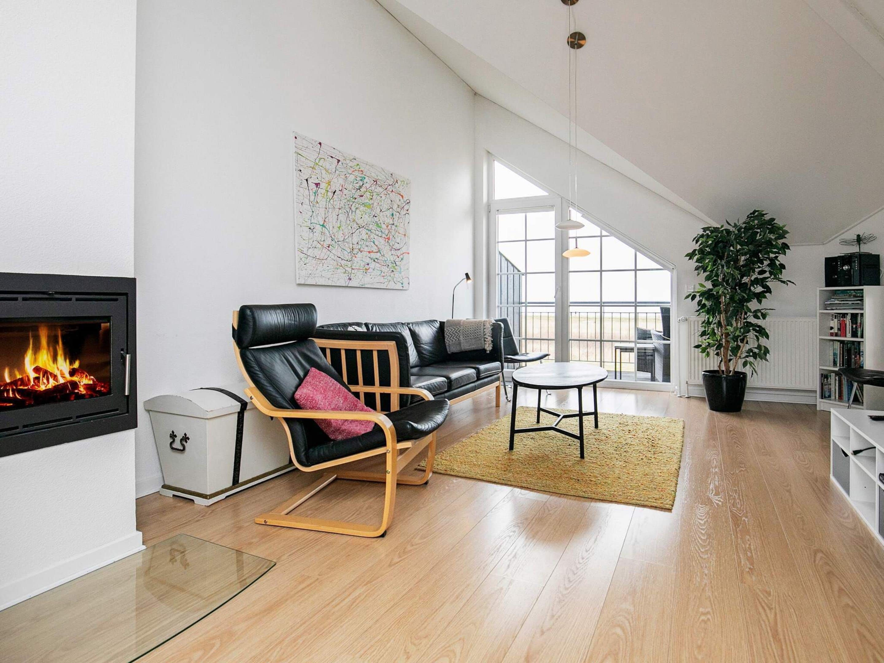 A modern living room with a fireplace, a black leather sofa, a wooden coffee table, and a large window offering a view of the outdoors.