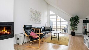 Una sala moderna con chimenea, un sofá de cuero negro, una mesa de centro de madera y un ventanal con vistas al exterior.