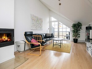 A modern living room with a fireplace, a black leather sofa, a wooden coffee table, and a large window offering a view of the outdoors. - 8 Person Holiday Park Home in Bogense (Bogense)