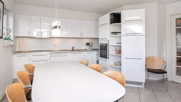 Una cocina moderna con armarios blancos, una isla central con sillas y electrodomésticos integrados.