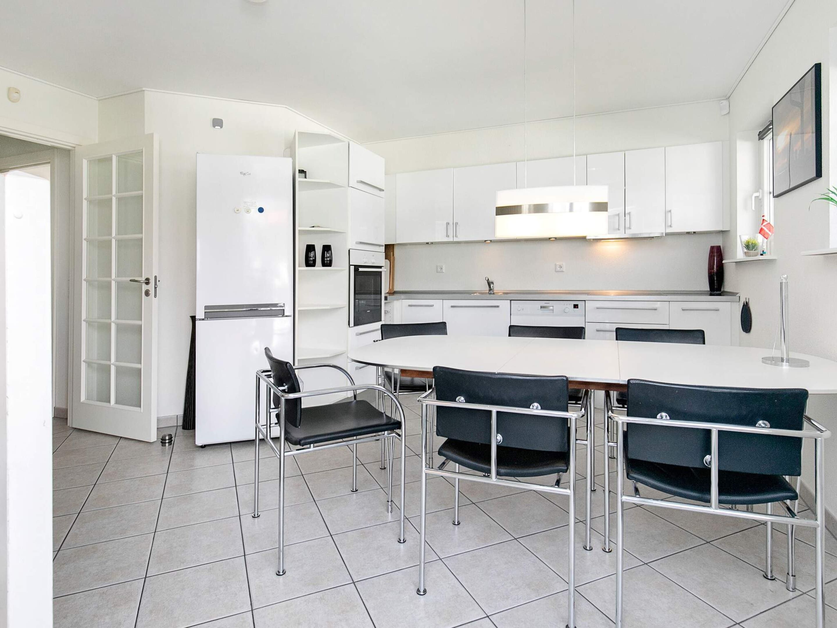 A modern kitchen with white cabinetry, a built-in oven, and a dining area with a round table and four chairs.
