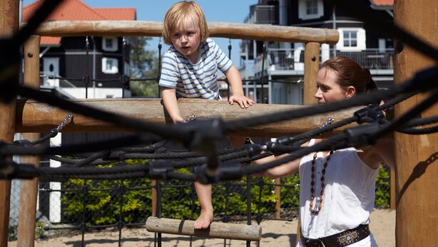Ein Spielplatz mit einer Seilbrücke und einem Kind, das darüber klettert.