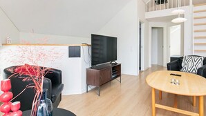 Una sala de estar moderna con una televisión de pantalla plana, piso de madera, una mesa de comedor y una escalera que lleva a un nivel superior.