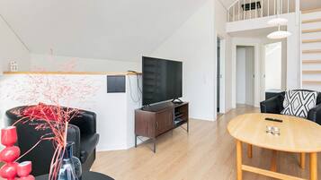 Een moderne woonkamer met een flatscreen-tv, houten vloeren, een eettafel en een trap naar een hoger gelegen verdieping.