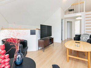 A modern living room with a flat-screen TV, wooden flooring, a dining table, and a staircase leading to an upper level. - 8 Person Holiday Park Home in Bogense (Bogense)
