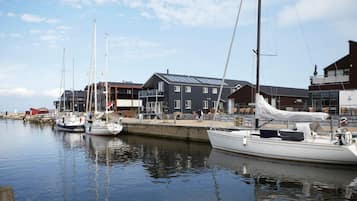 A marina with several sailboats docked, a modern building with a sloped roof, and a person cycling on the dock.