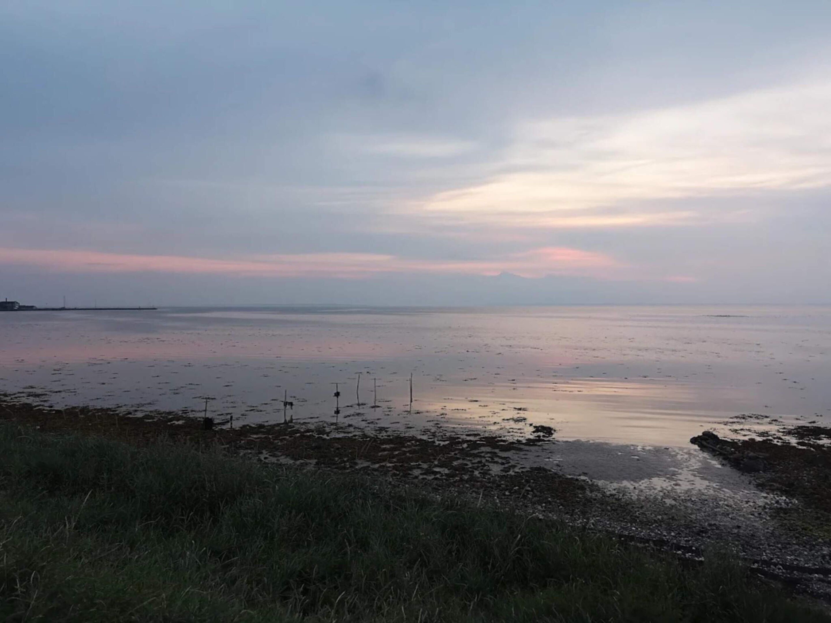 A coastal landscape with a calm sea, grassy foreground, and a distant shoreline.