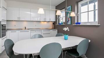 A modern kitchen with white cabinets, a white dining table, and blue chairs.