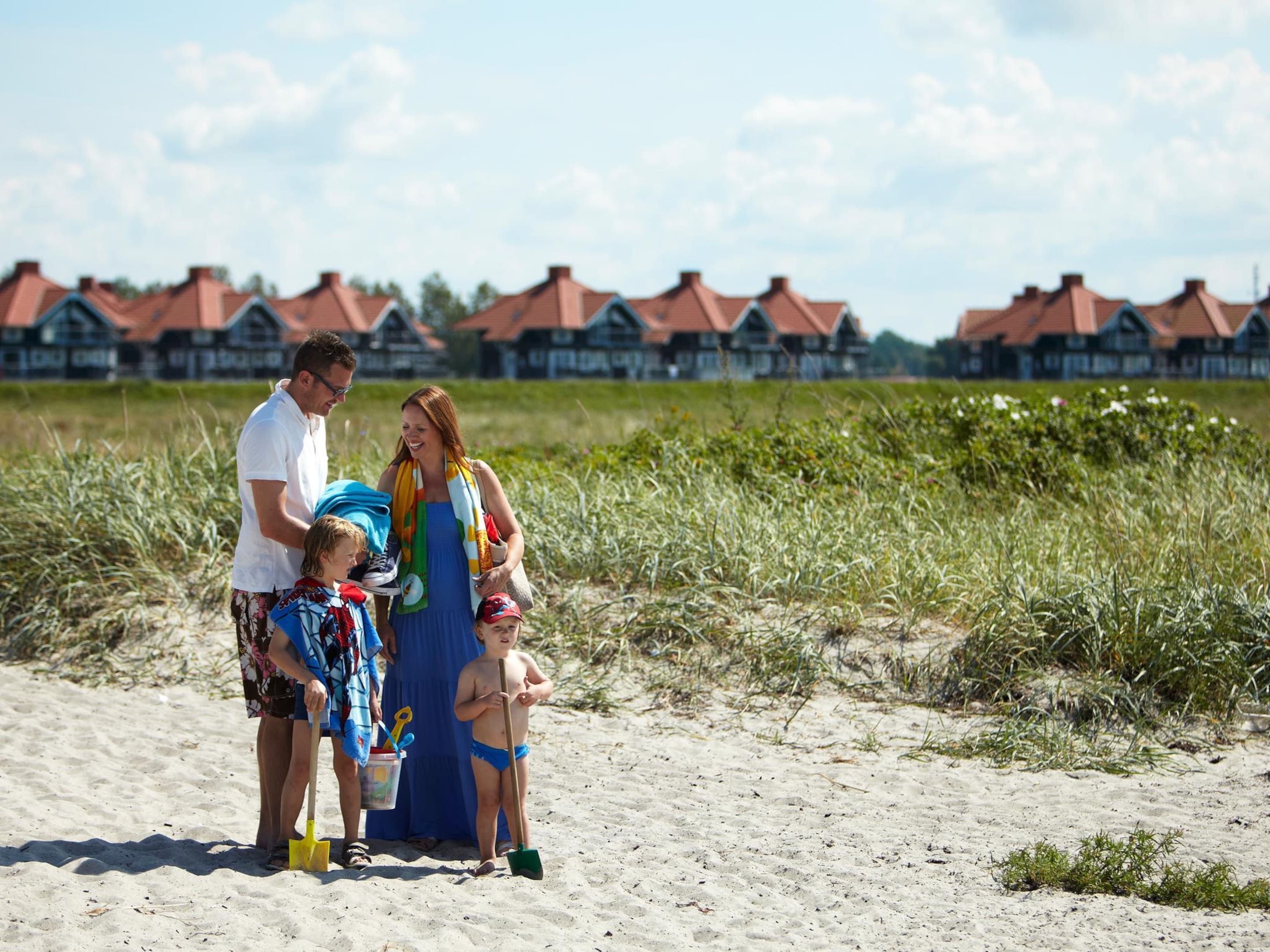 A family on a sandy beach with houses in the background.