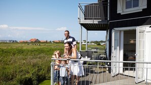 Eine Familie steht auf einem Balkon mit Blick auf ein grünes Feld und entfernte Gebäude.