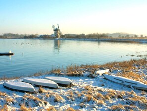 A calm lake with a windmill in the distance, surrounded by snow-covered ground and a few boats. - 8 Person Holiday Park Home in Bogense (Bogense)