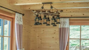 A wooden cabin with a dining table and chairs, checkered curtains, and a hanging light fixture. - Hackihutte Mountain hut (Rangersdorf)