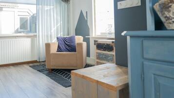A room with a beige armchair, a wooden table, a radiator, and a window with curtains.