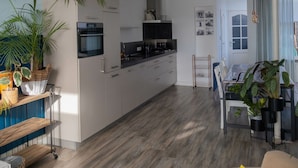 Une cuisine moderne avec des armoires blanches, un comptoir noir et un four encastré. On y trouve un coin repas avec une table et des chaises, ainsi qu'une grande plante en pot.