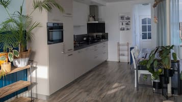 A modern kitchen with white cabinets, a black countertop, and a built-in oven. There is a dining area with a table and chairs, and a large potted plant.