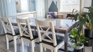 Un coin repas avec une table à plateau en verre, des chaises blanches et des plantes en pot.